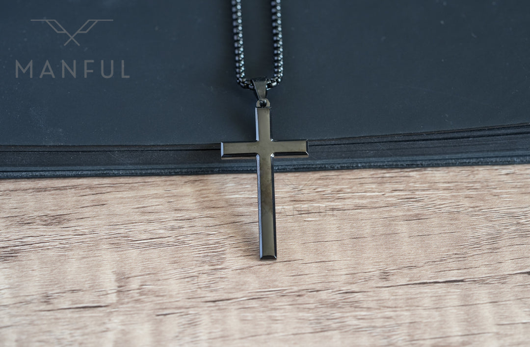 Cross Pendant Necklace Black, hanging against a black book edge on a wood surface