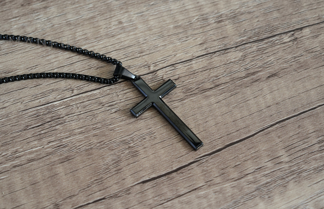 Cross Pendant Necklace Black, lying flat on a wood surface with the chain coiled beside it
