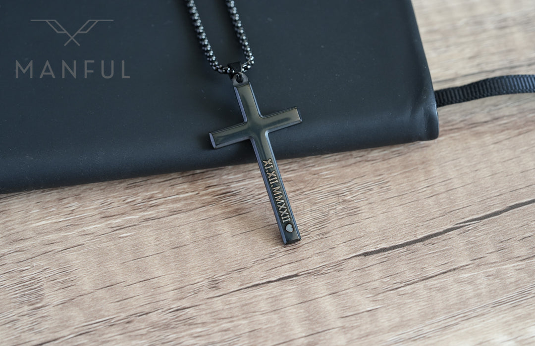 Cross Pendant Necklace Black, resting against a black pouch on wood showing the engraved side