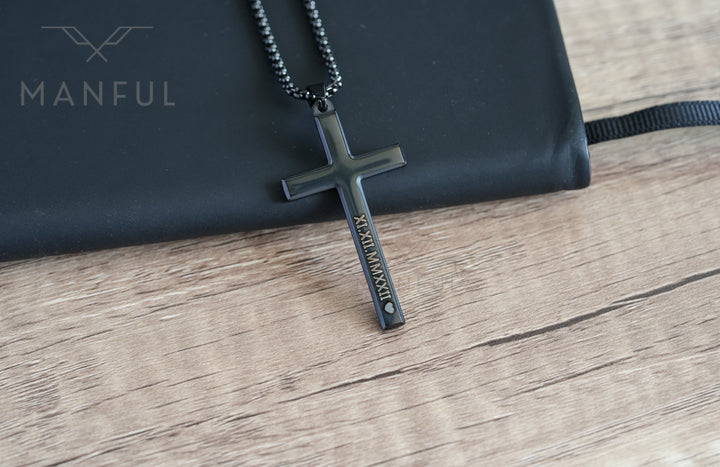 Cross Pendant Necklace Black, resting against a black pouch on wood showing the engraved side