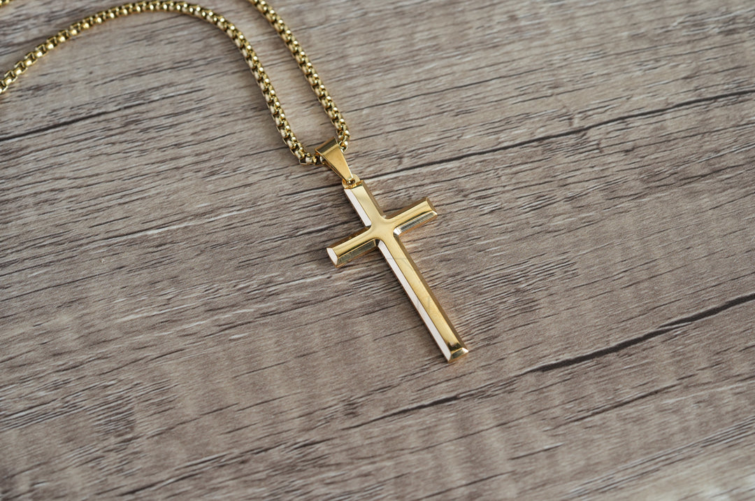 Cross Pendant Necklace Gold, laid diagonally on a wood surface with the chain coiled above