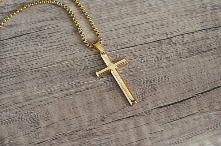 Cross Pendant Necklace Gold, laid diagonally on a wood surface with the chain coiled above