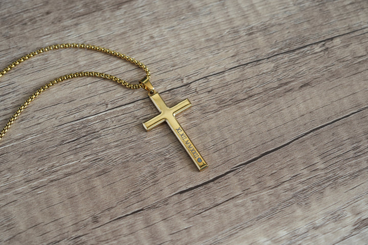 Cross Pendant Necklace Gold, close-up on wood showing a small engraving along the vertical bar