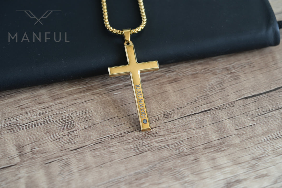 Cross Pendant Necklace Gold, laid on wood beside a dark pouch showing the engraving and a tiny stone accent