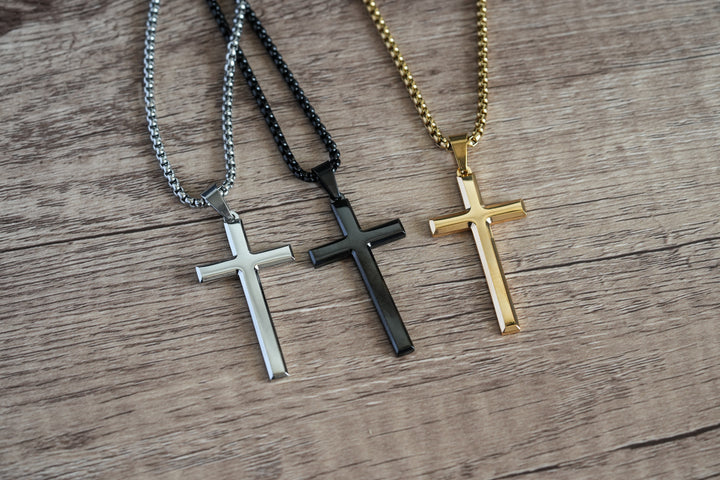Cross Pendant Necklace Gold, laid on wood beside the matching silver and black colour variants
