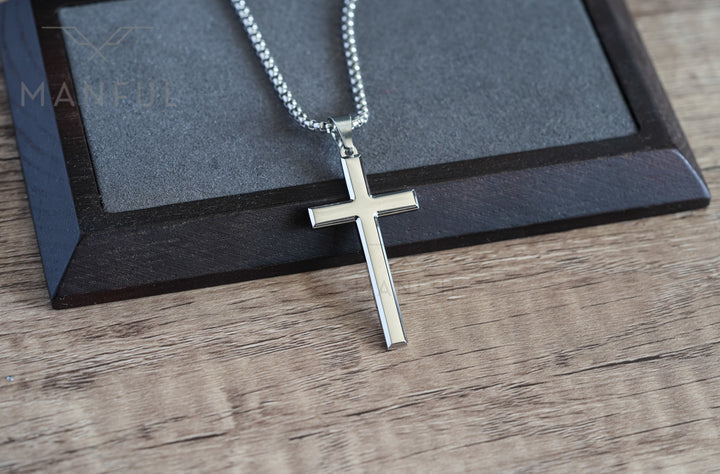 Cross Pendant Necklace Silver, resting on a wood surface beside a dark leather-bound box