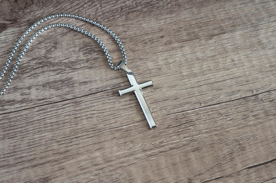 Cross Pendant Necklace Silver, flat lay on a wood surface with the chain looped above it