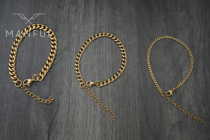 Cuban Chain Bracelet Gold, displayed as three curb-link bracelets on a wood surface