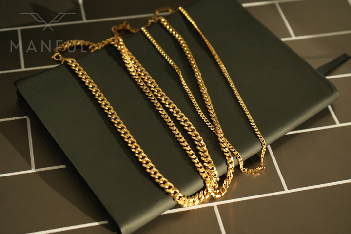 Cuban Chain 5mm Gold, several lengths draped together over a black pouch on tiled flooring