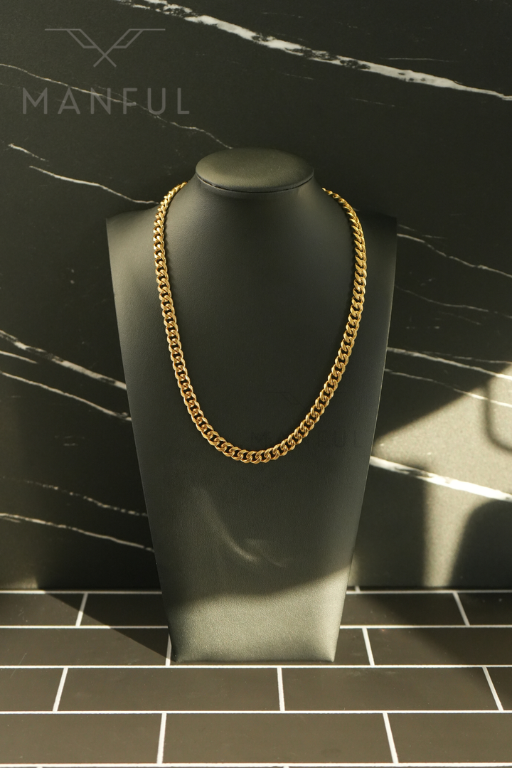Cuban Chain 7mm Gold, worn on a dark display bust against a marble tile floor