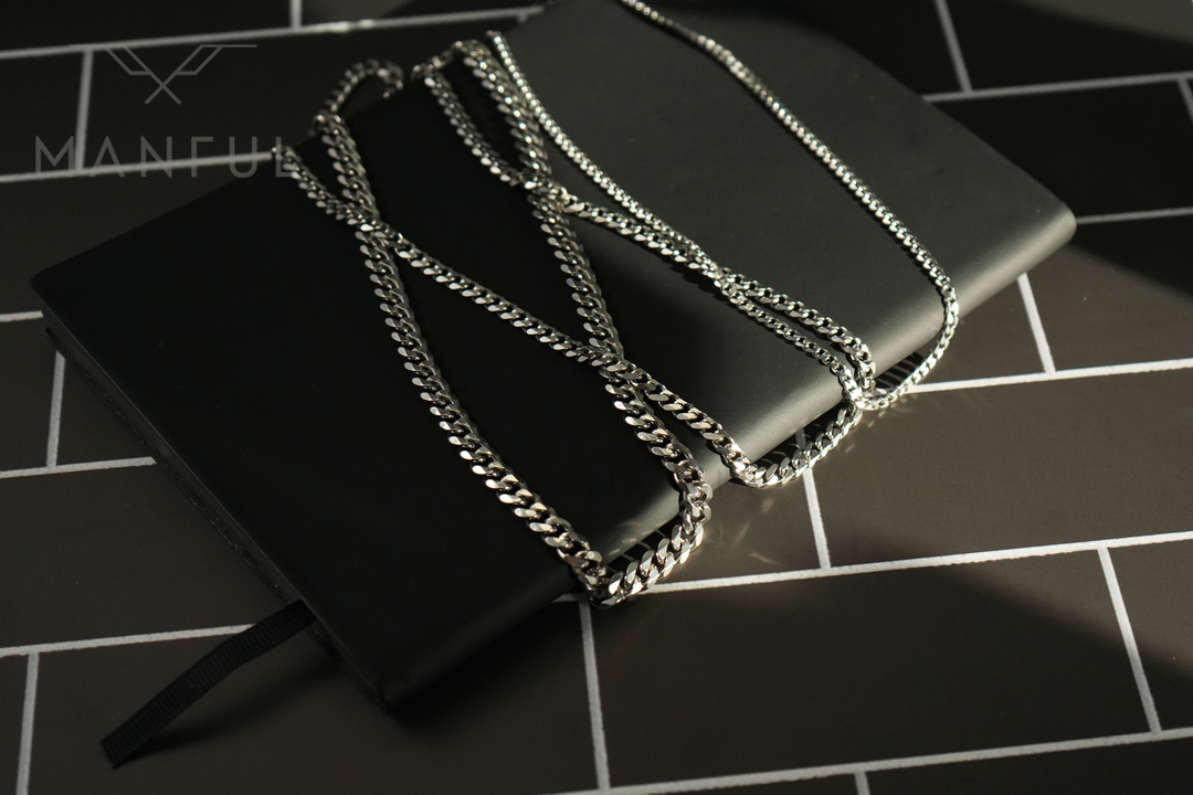 Cuban Chain 3mm Silver, draped over a black notebook on a dark tiled floor
