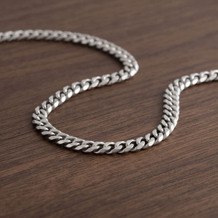 Cuban Chain 5mm Silver lying in a loose curve on a walnut table