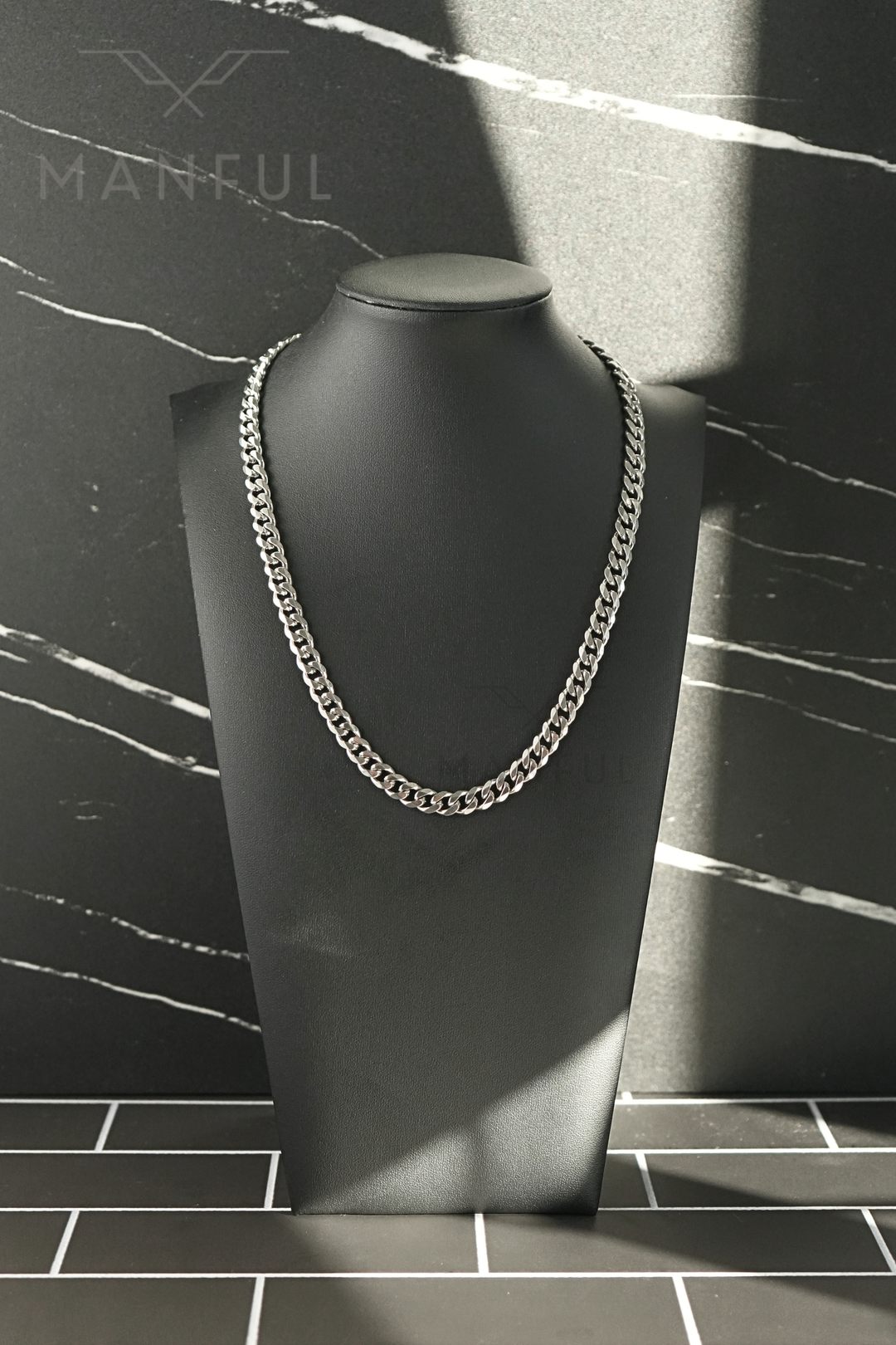 Cuban Chain 7mm Silver, worn on a black display bust against a marble backdrop with a light beam