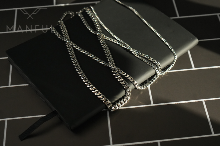 Cuban Chain 7mm Silver, draped across a black leather notebook on a tiled floor