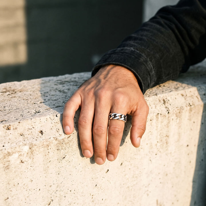 Cuban Chain Ring (Silver) on a man's finger, his hand resting on a concrete ledge