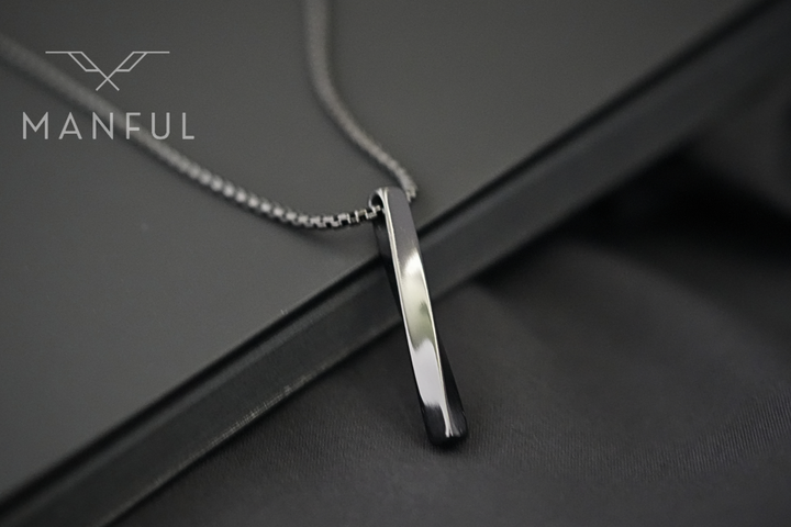 Cuboid Pendant Chain Black, close-up resting diagonally on a dark leather surface