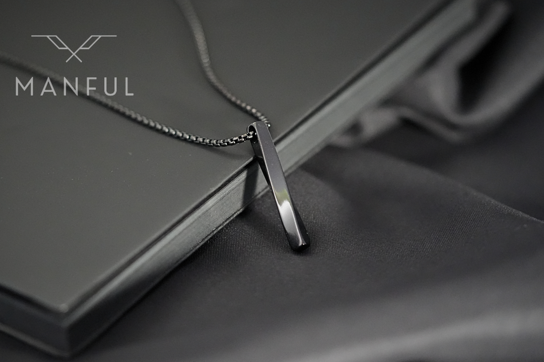Cuboid Pendant Chain Black, close-up leaning against a black book on dark fabric