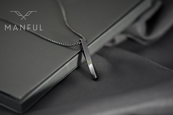 Cuboid Pendant Chain Black, close-up leaning against a black book on dark fabric