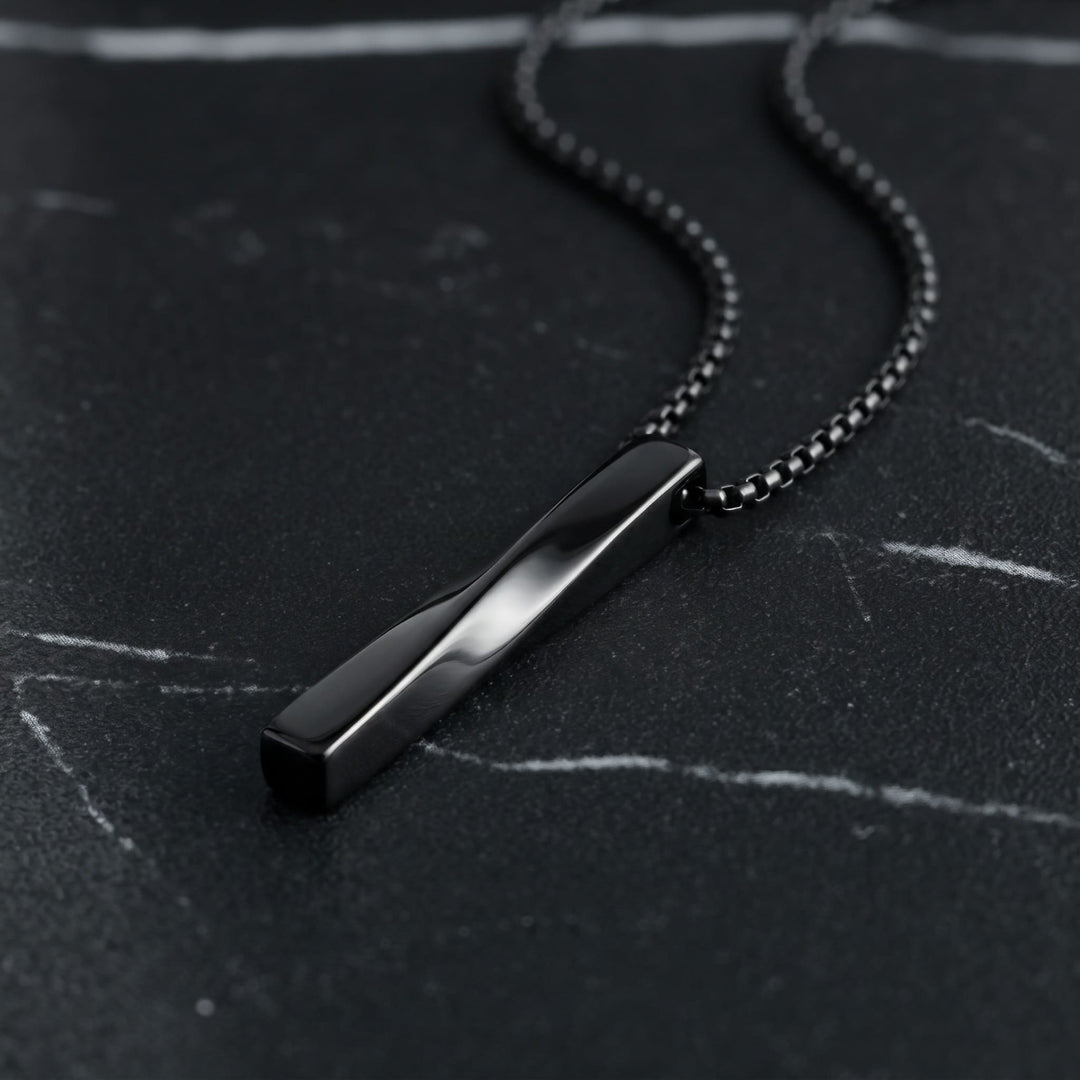 Cuboid Pendant Chain (Black) lying on dark marble with the chain curving behind it