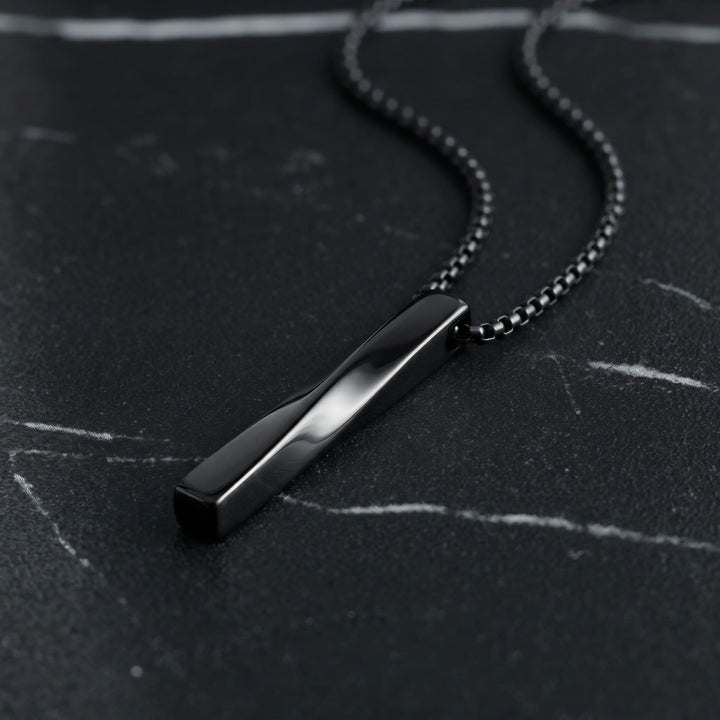 Cuboid Pendant Chain (Black) lying on dark marble with the chain curving behind it