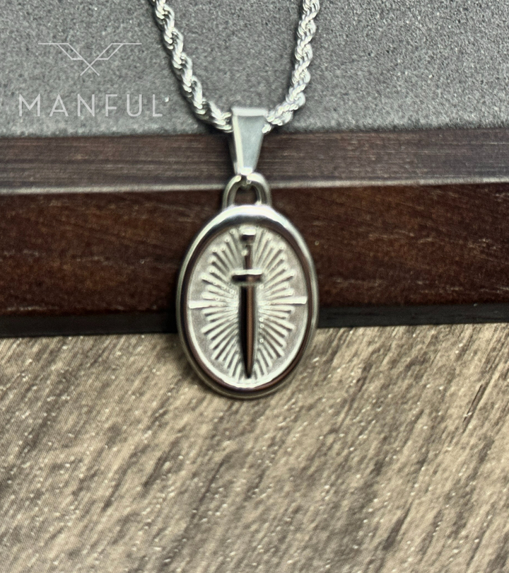 Dagger Emblem Pendant Necklace Silver, close-up resting against a dark wood block on a wood table