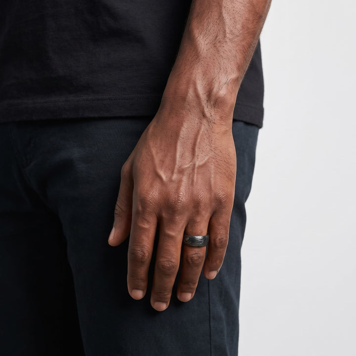 Damascus Steel Band (Black) on a man's finger, his hand hanging at his side