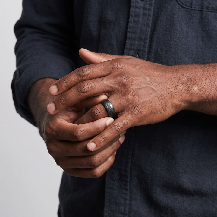 Damascus Steel Band (Black) on a man's finger as his other hand turns it