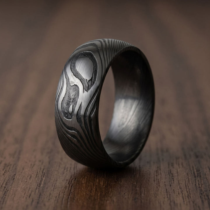 Damascus Steel Band (Black) standing on a walnut table with the grain pattern facing out
