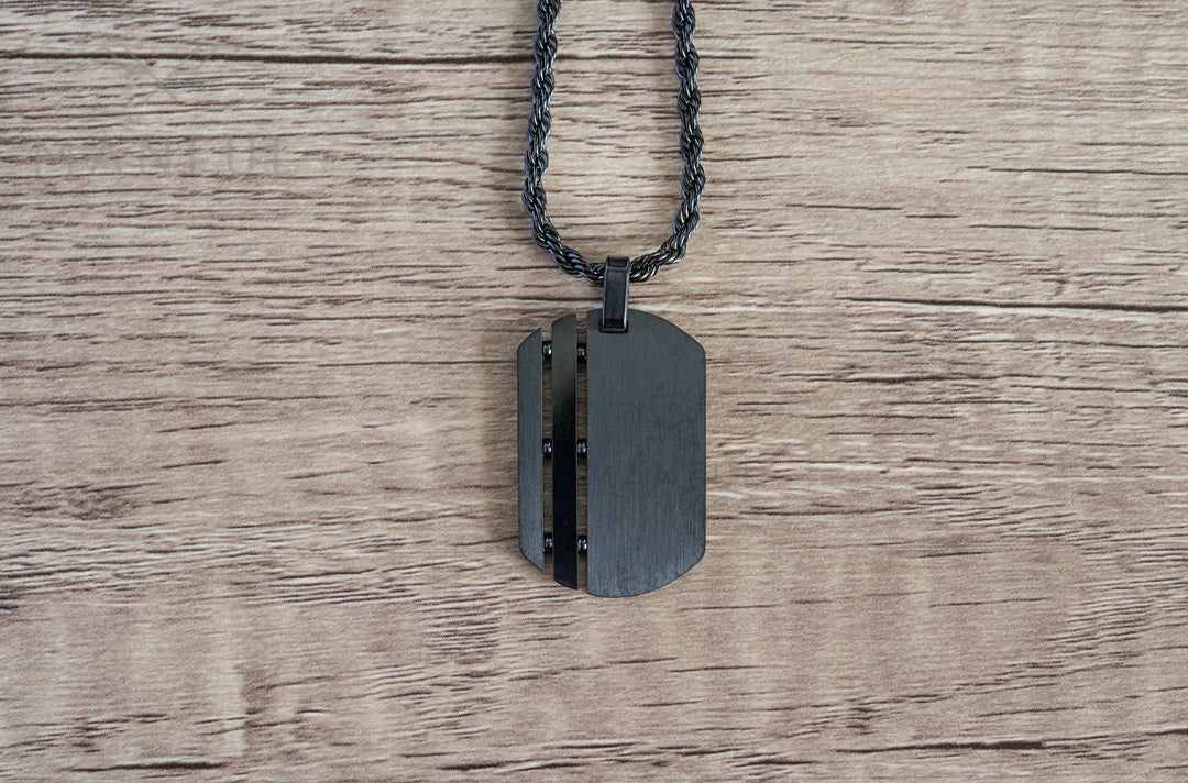 Dog Tag Chain Black, laid flat on a wood surface with the chain coiled above it