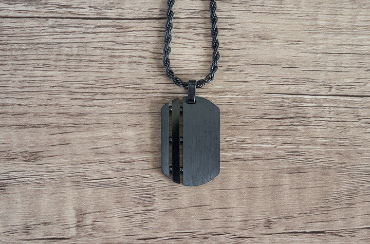 Dog Tag Chain Black, laid flat on a wood surface with the chain coiled above it