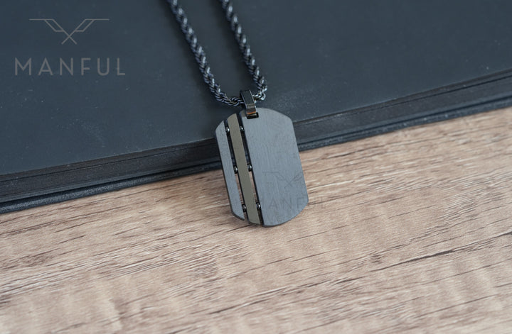 Dog Tag Chain Black, propped against a black book on a wood surface, close-up angle
