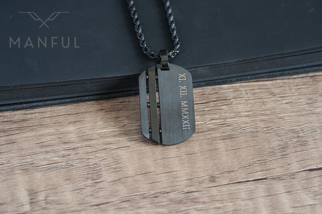 Dog Tag Chain Black, propped on a black book showing the engraved roman numeral date