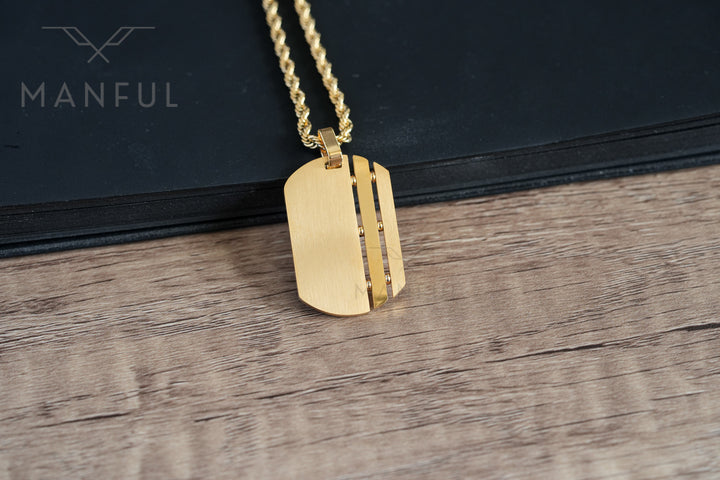 Dog Tag Chain Gold, resting against a black book on a wood surface with the chain draped down