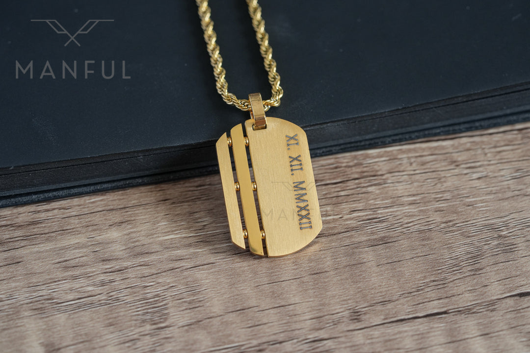 Dog Tag Chain Gold, close-up on a black book showing a custom roman numeral date engraving