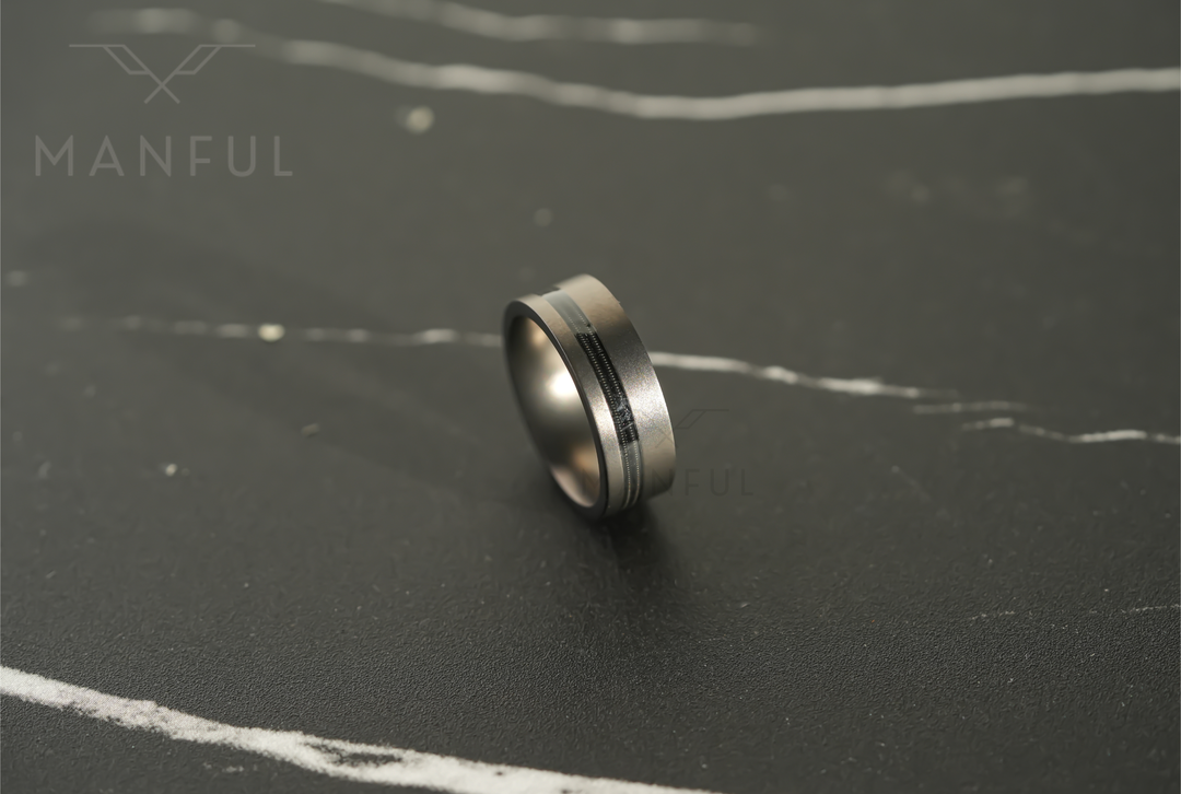 Gunmetal Guitar String Tungsten Band, resting at an angle on a dark marble surface