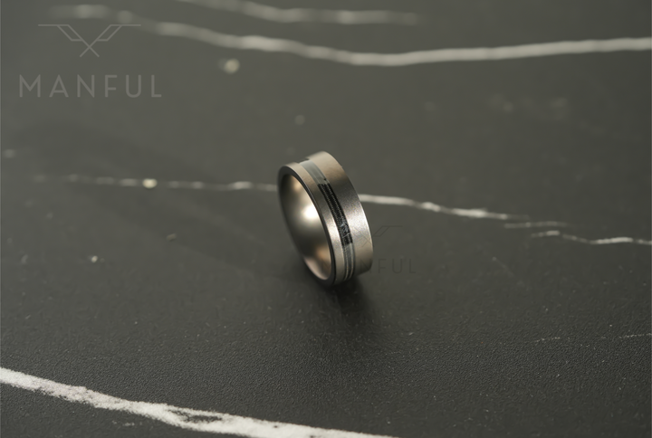 Gunmetal Guitar String Tungsten Band, resting at an angle on a dark marble surface