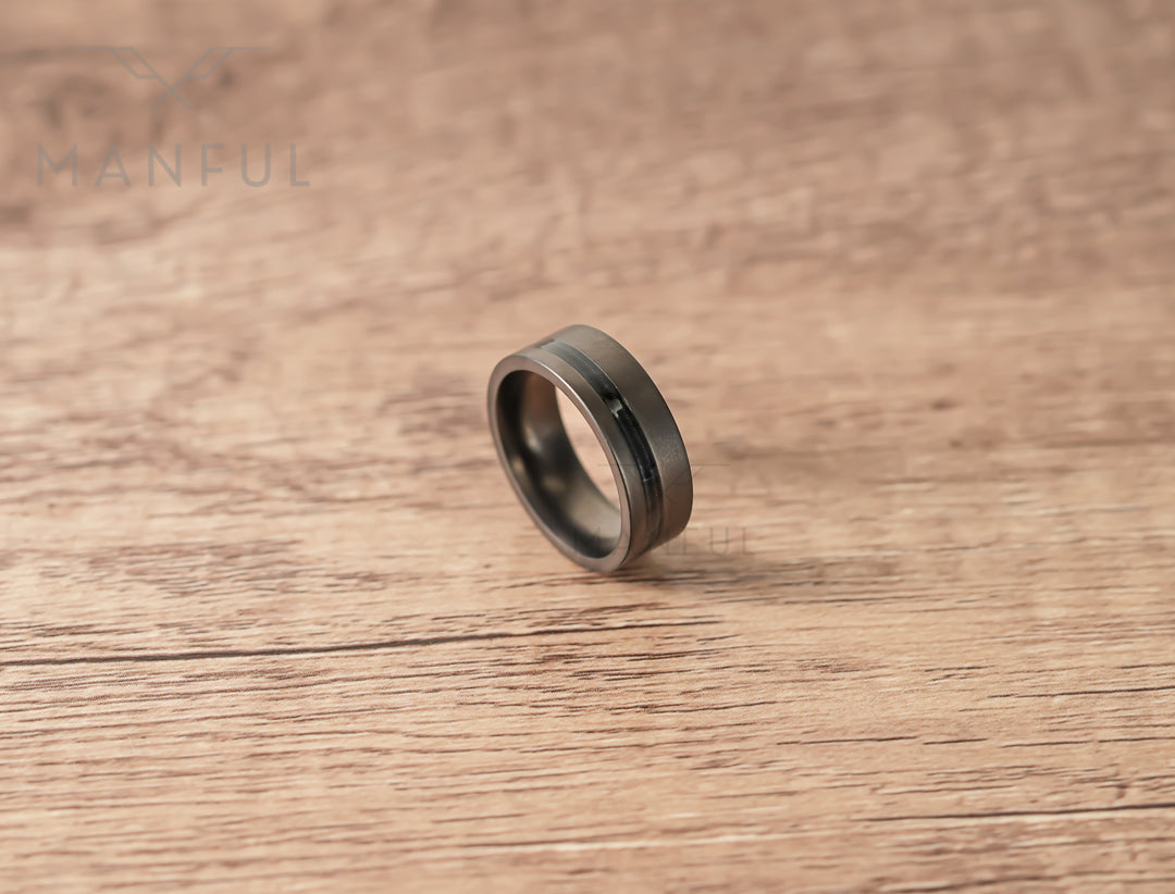 Gunmetal Guitar String Tungsten Band, angled on a wooden table with the wire inlay catching the light