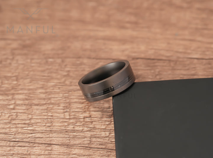 Gunmetal Guitar String Tungsten Band, propped against a black block on a wooden table