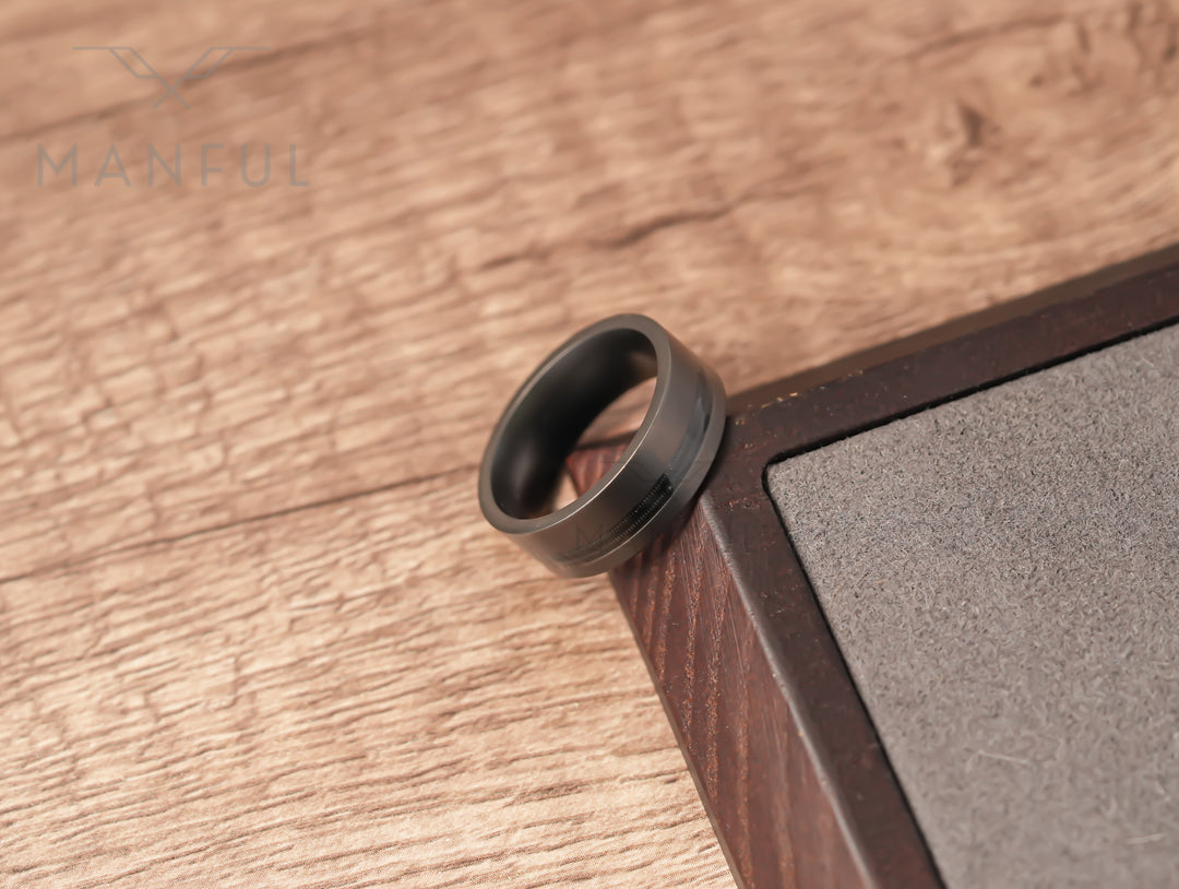 Gunmetal Guitar String Tungsten Band, resting in the corner of a two-tone wooden block