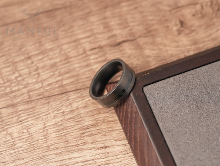 Gunmetal Guitar String Tungsten Band, resting in the corner of a two-tone wooden block