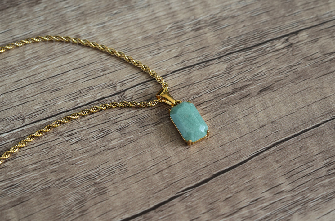 Jade Stone Pendant Gold, laid on a wooden surface with the chain curving beside it