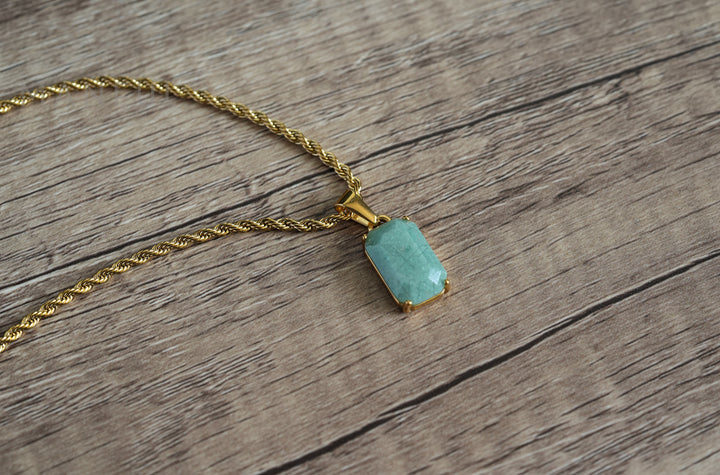 Jade Stone Pendant Gold, laid on a wooden surface with the chain curving beside it