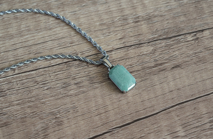 Jade Stone Pendant Silver, laid diagonally on a wood surface with the chain coiled to the side