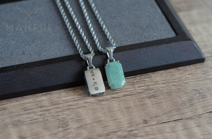 Jade Stone Pendant Silver, laid on wood beside a matching engraved silver tag pendant