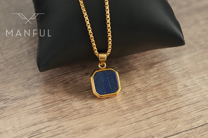 Lapis Square Necklace Gold, resting against a black leather cushion on a wood surface