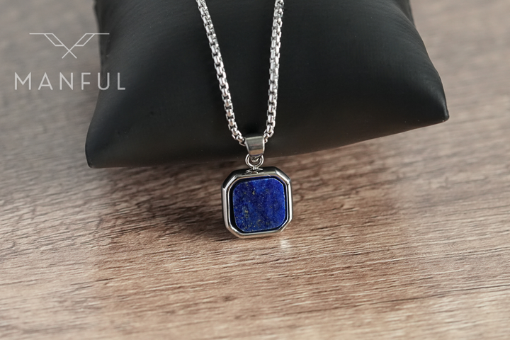 Lapis Square Necklace Silver, draped over a black leather cushion on a wood surface