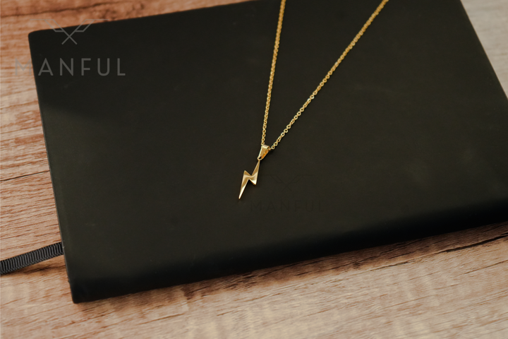 Lightning Pendant Necklace Gold, draped over a black book on a wood surface