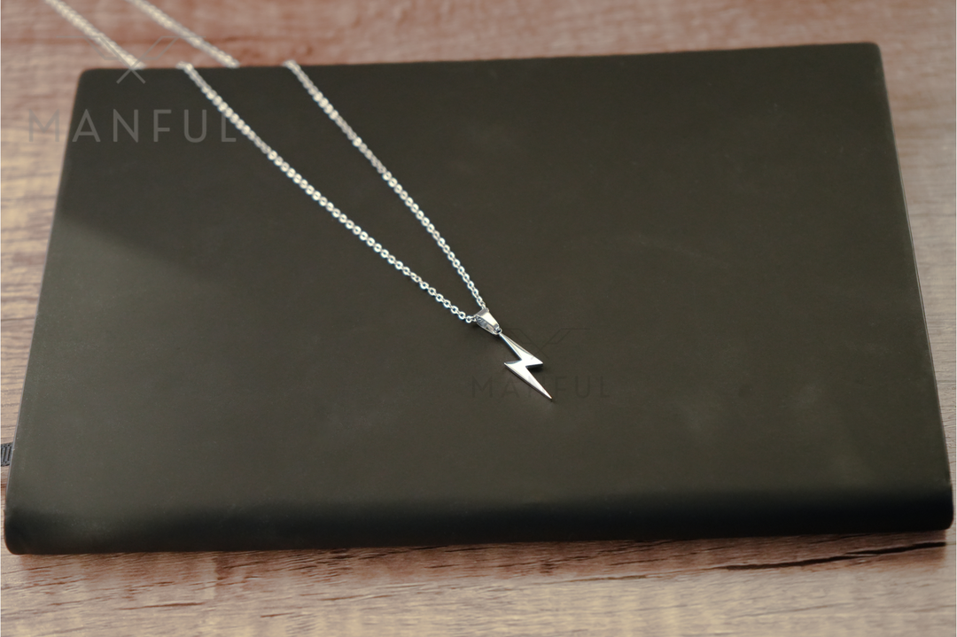 Lightning Pendant Necklace Silver, chain and bolt pendant laid across a black book on wood