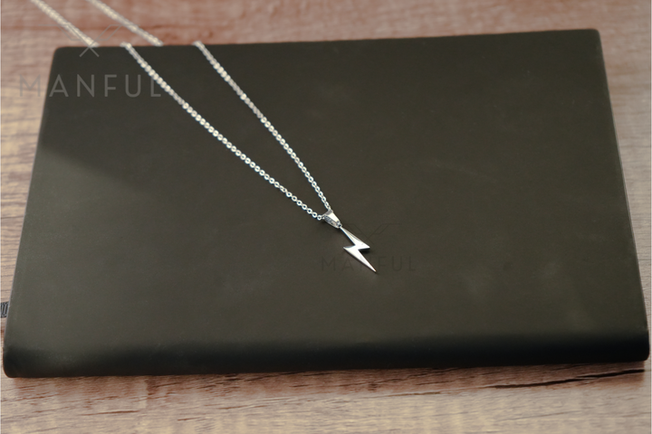 Lightning Pendant Necklace Silver, chain and bolt pendant laid across a black book on wood