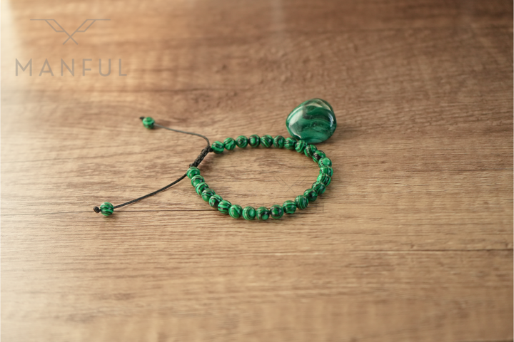 Malachite Bead Bracelet, laid flat on a wood table beside a loose malachite stone